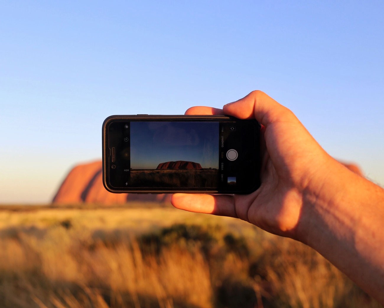 mano con teléfono móvil mostrando en pantalla la montaña sagrada de Uluru de Australia